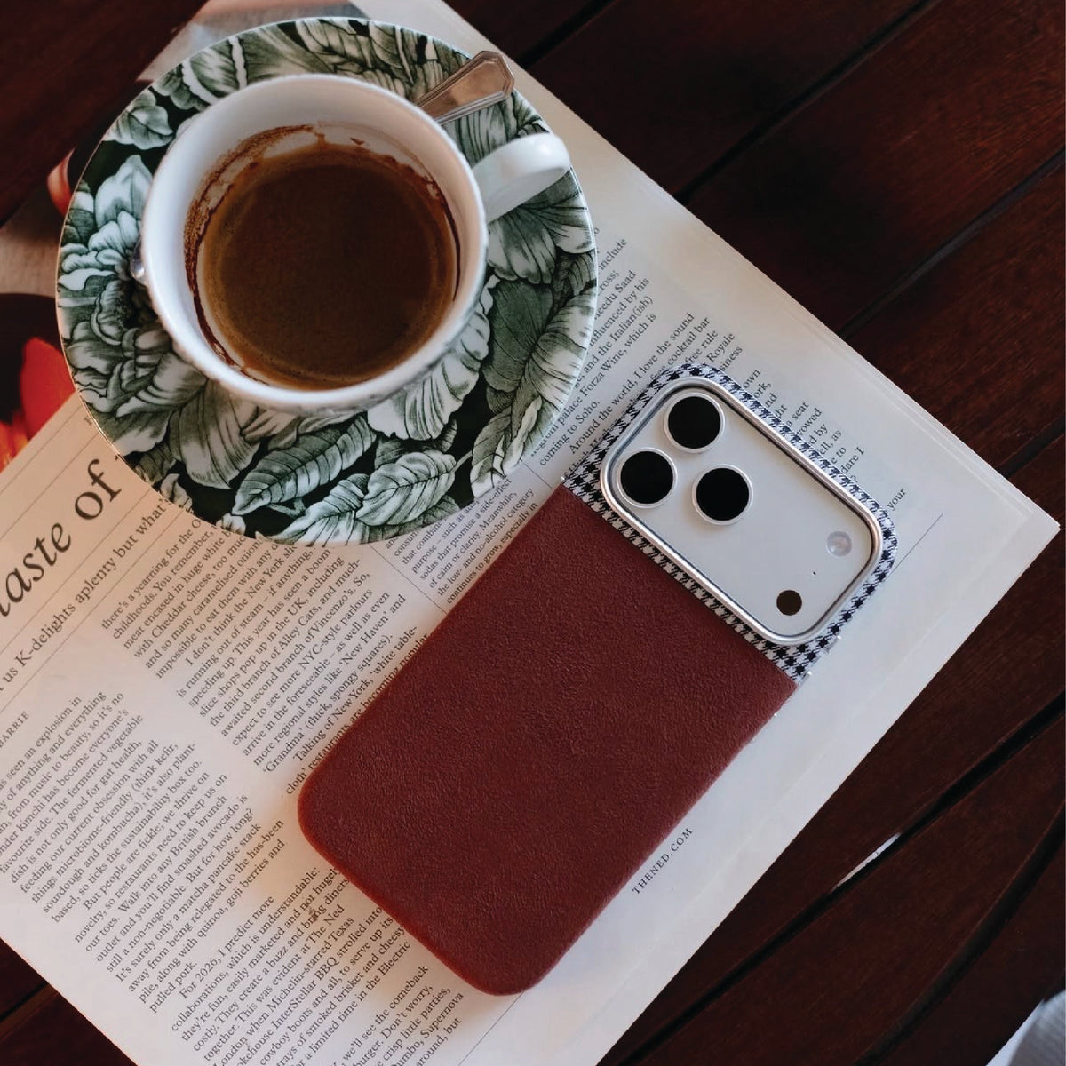 A pepita phone case on a book beside a coffee cup