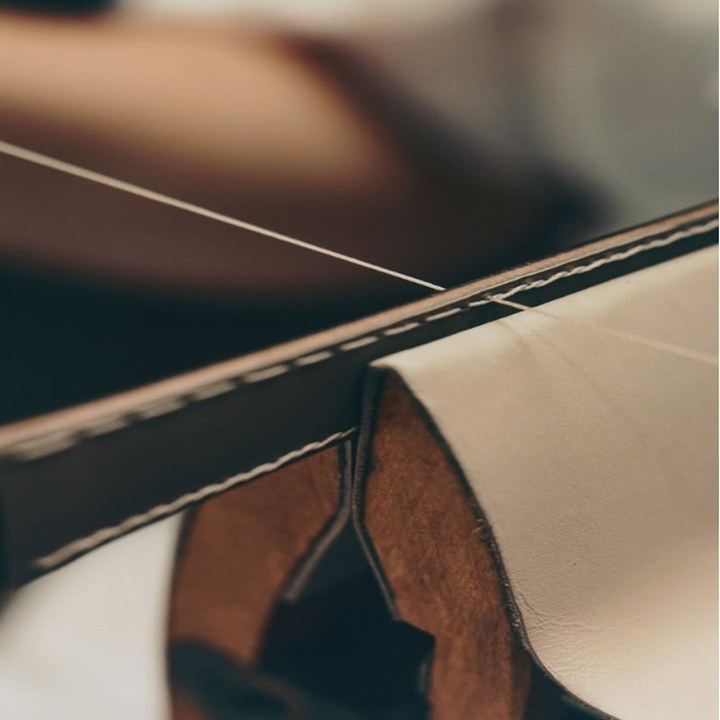 Elemento atelier — a needle drawing thread through a leather edge
